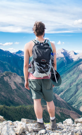 Мущина, стоящий на горе и смотрящий на долину.